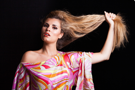 blonde girl beauty portrait hold her long hair in hand wearing colorful silky dress studio shotの写真素材