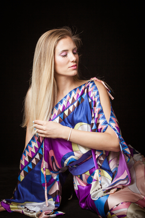 beauty young blonde woman portrait with interesting  makeup eyelashes and crystals in colorful silky dress studio shotの写真素材