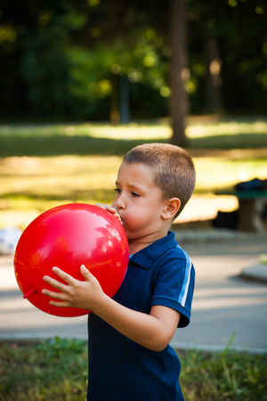 little boy inflate big red  balloon in park summer dayの写真素材