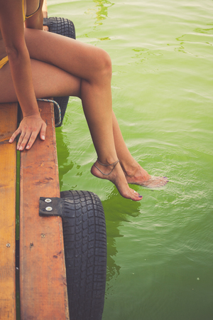 young woman sit on wooden dock by river or lake cooling feet in clear water hot summer dayの写真素材