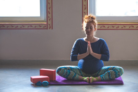 red head pregnant young woman on yoga class indoor meditationの写真素材