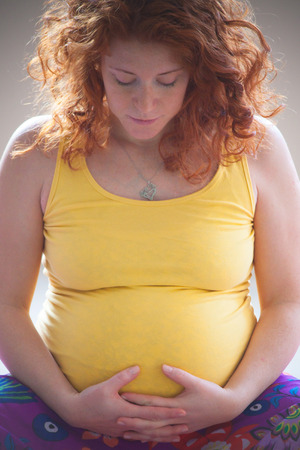 red hair young pregnant woman hold her belly indoor shot natural lightの写真素材