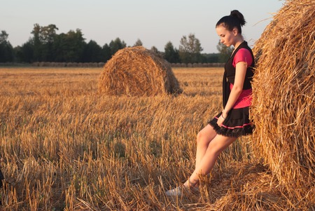 The girl in the skirt is posing near a bale of strawの写真素材