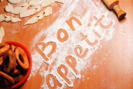 The inscription bon appetit on the table with flour, dough and donutsの写真素材