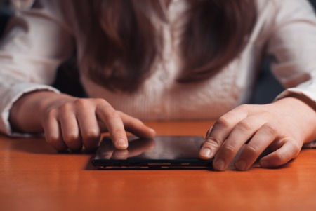 young girl works on the tablet at the table, surfing the Internetの写真素材