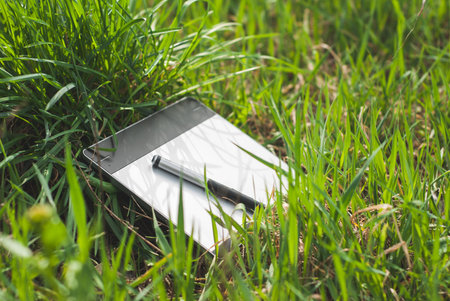a graphics tablet with a pen lying in the thick grass of spring