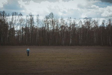 cowboy in the distance standing in a field on the background of the spring woods and sky with cloudsの写真素材