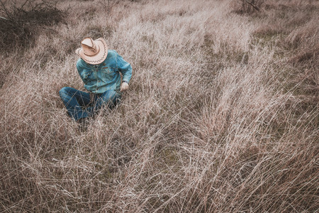 Cowboy sits on the dry grass, a Man in a cowboy hatの写真素材