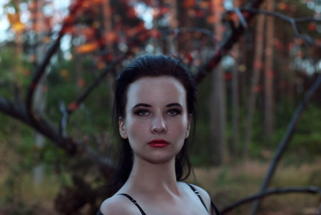 a young witch in the woods, a woman in a dark dress on a background of old branches, the mage uses...