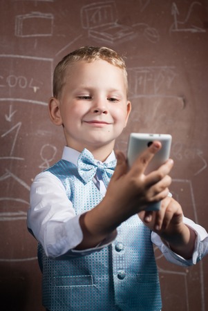 Little schoolboy makes a selfie, boy in suit on the background of the school Board, the young blonde with the phoneの写真素材