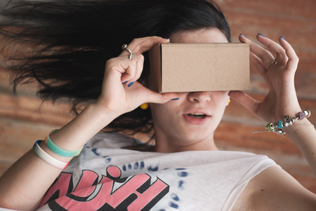 Young girl having fun playing with your cardboard VR headset attached to her smartphone. playful girl in a white t-shirtの写真素材