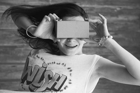 Young girl having fun playing with your cardboard VR headset attached to her smartphone. playful girl in a white t-shirtの写真素材