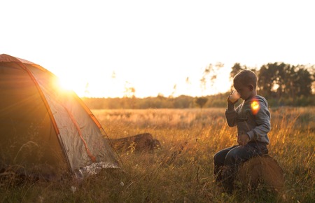 boy drinking juice at sunset, boy sitting near tent silhouette shootingの写真素材