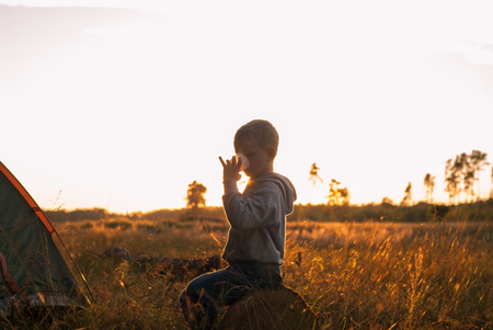 boy drinking juice at sunset, boy sitting near tent silhouette shootingの写真素材