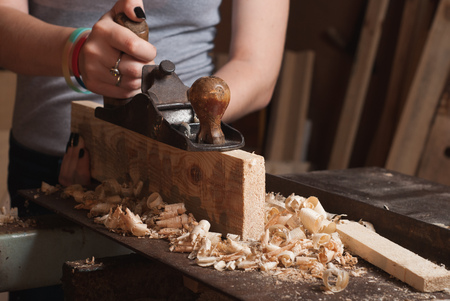the carpenter in the workshop, the chips on the table, the girl works with a planeの写真素材