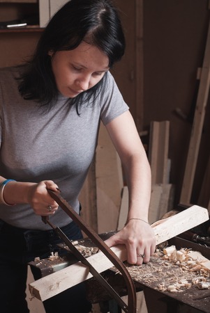 the girl sawing lumber, the carpenter works in a workshopの写真素材