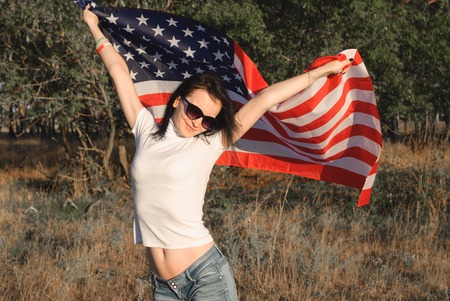 The girl with the American flag outdoors, stars and stripes flag flutters in the wind, happy patriot's dayの写真素材