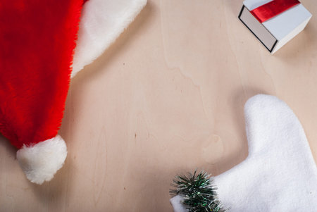Red Santa hat, branch tree, Christmas socks and white gift with red ribbon on wooden background,...
