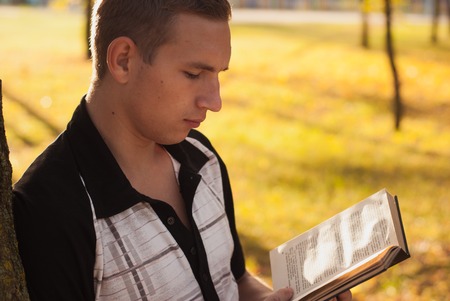 Young man reading book in autumn Park, yellow leaves, welcome autumnの写真素材