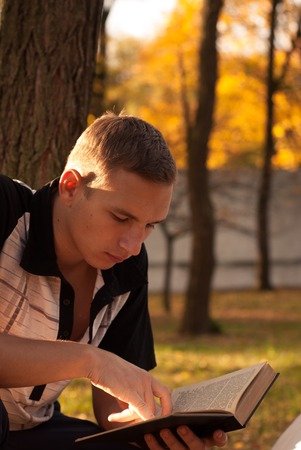 Young man reading book in autumn Park, yellow leaves, welcome autumnの写真素材