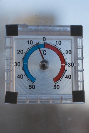 below zero on the old analogue thermometer,the concept of cold weather, the thermometer outside the window, frost on the yardの写真素材