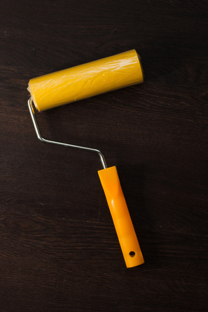 Yellow paint roller on a dark background, wood texture, repair toolの写真素材