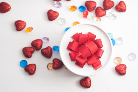 Round box with red bow, view from the top, scattered red hearts and decorative stones, Valentine's day, festive backgroundの写真素材