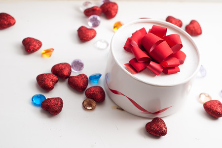 Round box with red bow, scattered red hearts and decorative stones, Valentine's day, festive backgroundの写真素材