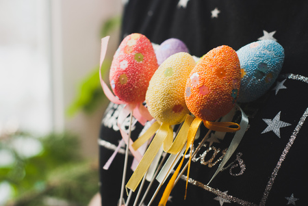 Girl in a dark jacket holding Easter eggs on a stickの写真素材