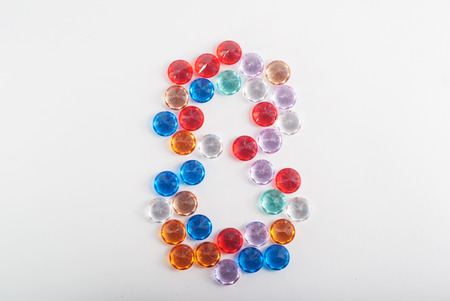 Multicolored faceted stones in the shape of the number 8 on a white background, international women's day, the figure 8の写真素材