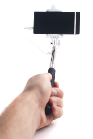 Man's hand holds a selfie stick with a connected smartphone, isolated on white background, youth gadget, mobile photography, device for hipsterの写真素材
