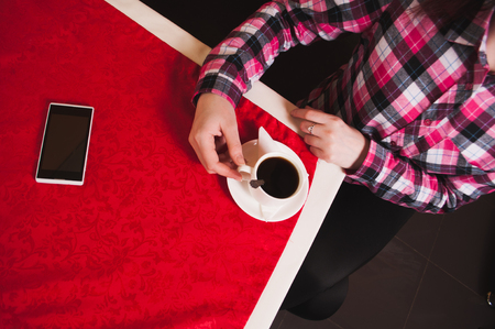 Female hands holding Cup of coffee on the table with a red tablecloth, white smartphone,の写真素材