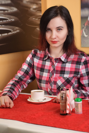 Girl in a plaid shirt drinking coffee, young woman in cafe, red lipstick, beautiful brunetteの写真素材