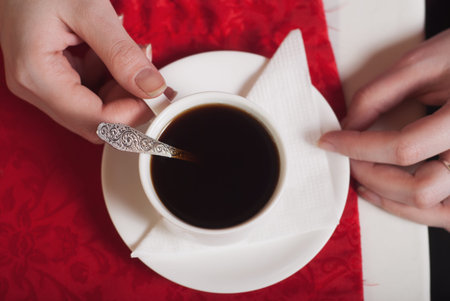 Female hands holding a Cup of black coffee on the table with a red tablecloth, top view