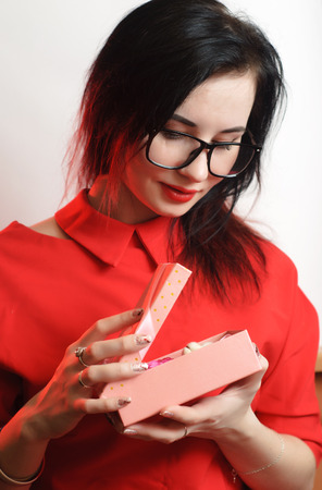 Closeup portrait of female model in red dress on white background, cute brunette with black glasses, opens gift, women's day March 8の写真素材