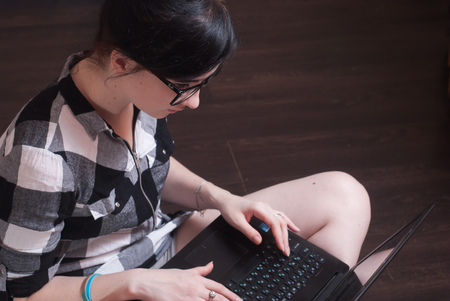 young woman brunetka sitting on the floor with crossed legs and typing on the laptopの写真素材