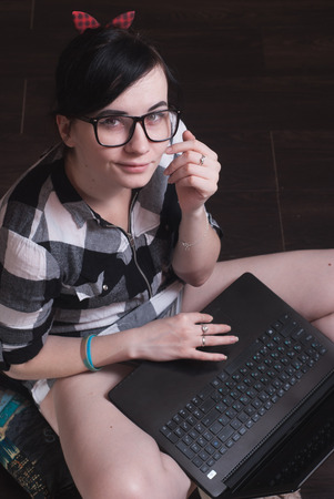 young woman brunetka sitting on the floor with crossed legs and typing on the laptopの写真素材
