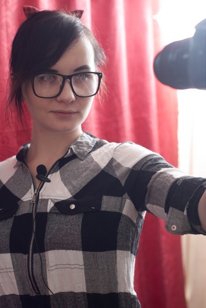 A young female blogger shoots himself on camera, cute brunette, hipser glasses, lifestyle vlog, red backgroundの写真素材