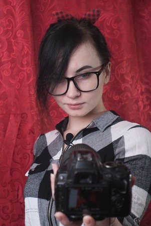 A young female blogger shoots himself on camera, cute brunette, hipser glasses, lifestyle vlog, red backgroundの写真素材