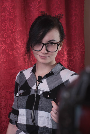 A young female blogger shoots himself on camera, cute brunette, hipser glasses, lifestyle vlog, red backgroundの写真素材