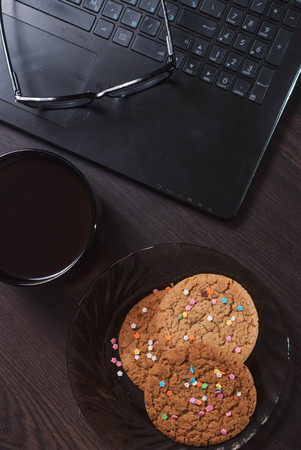 Workplace with laptop, Cup of hot coffee, glasses and biscuits, low key,の写真素材