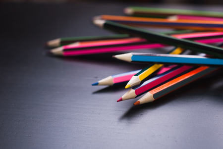 Colored pencils scattered on the Desk, black textured wood, copyspace, creative and messyの写真素材