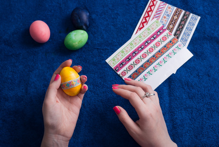 Easter eggs on blue background, female hands glued decorative tape on the yellow egg, preparing for Easterの写真素材