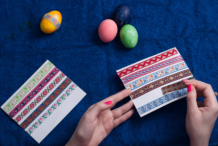 Easter eggs on blue background, female hand, labels with patterns, preparation for Easterの写真素材