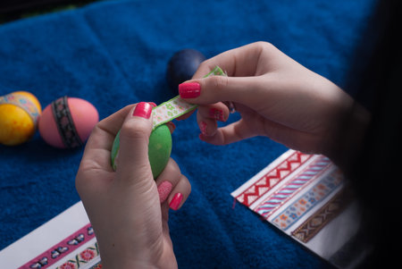 Easter eggs on blue background, female hands glued decorative tape on green egg, preparing for...