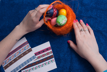 Female hands put Easter eggs in basket on blue background, view from topの写真素材