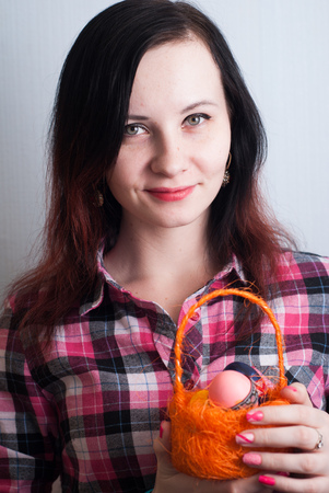 Girl hipster in a plaid shirt holding an orange basket with Easter eggs, a nice smile, a happy Easterの写真素材