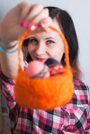 Girl hipster in a plaid shirt holding an orange in a basket full of Easter eggs, nice smile, happy Easter, look through the basket, an unusual perspectiveの写真素材