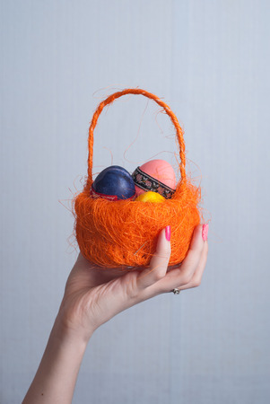Orange basket with eggs in female hand, pink nail Polish, pastel background, pattern for holiday cards, happy Easterの写真素材