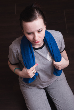 Young sporty woman after workout with towel on shoulders sitting on the floor, rest after exercise, towelの写真素材
